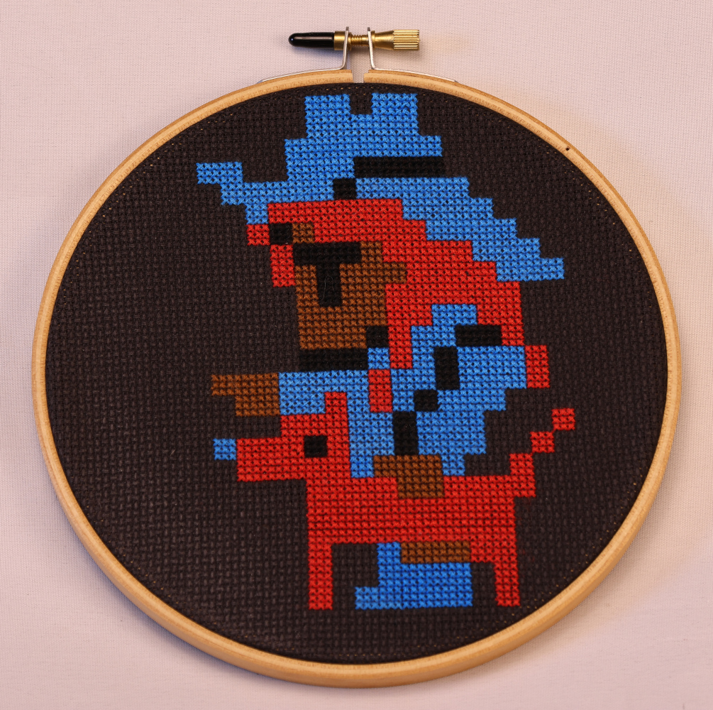Photograph of a cross stitch on black aida. A pixel-rendered beast master in the FF1 style with a cowboy hat, long red hair, blue clothes, a red dog, and brown skin. One of the beast master's hands rests on the dog's back, while the other points straight ahead.